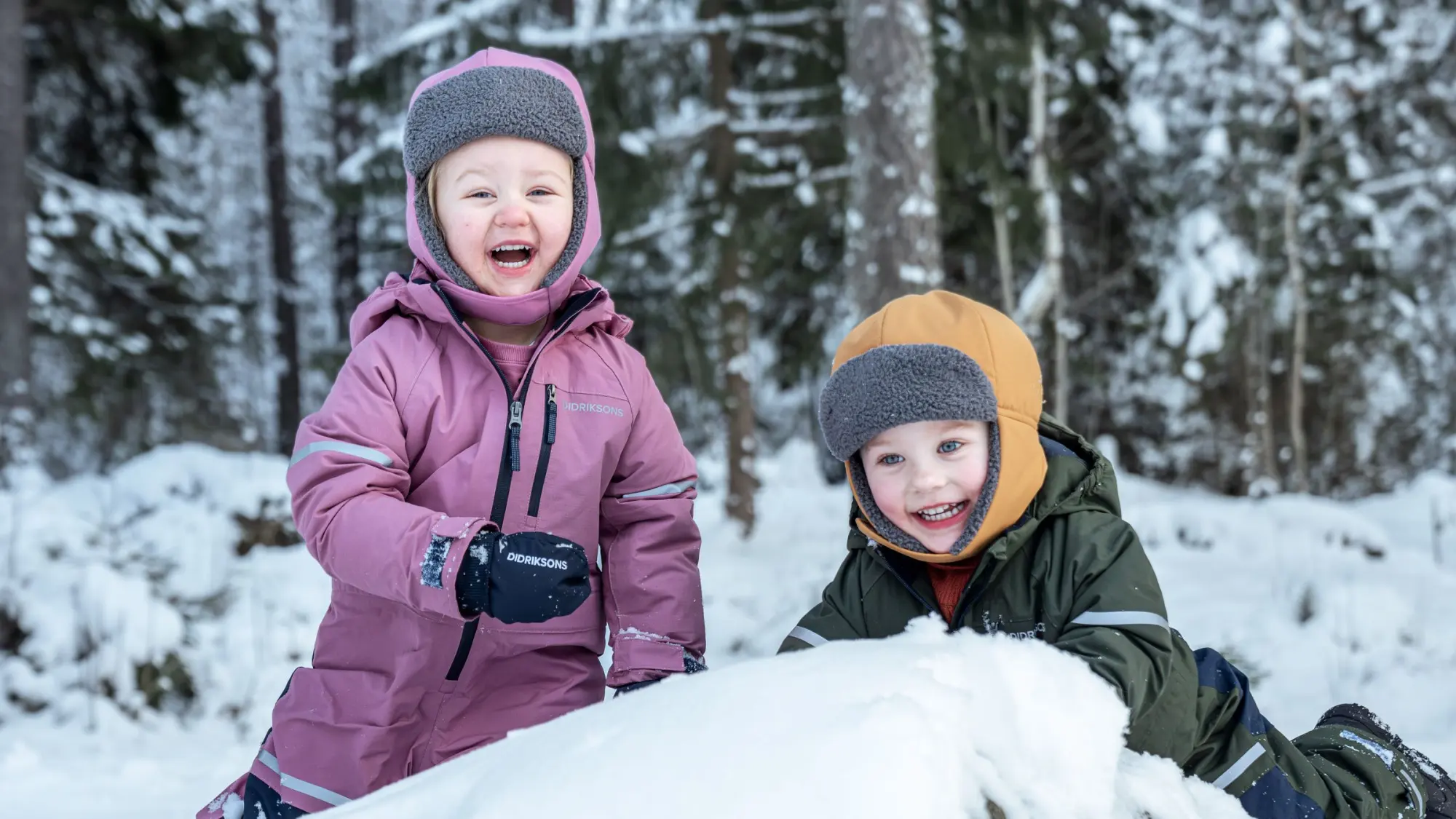 Två barn i vinteroveraller leker i snön